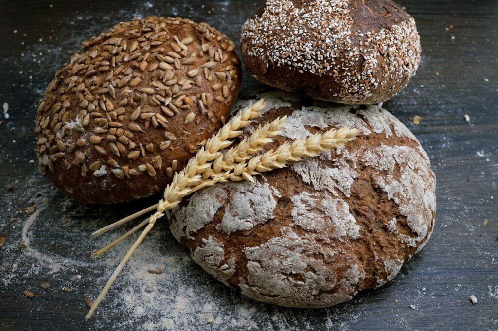 Three loaves of rustic bread with sunflower seeds and wheat stalks on wood